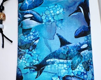 May include: A blue zippered pouch with a colorful print of orcas swimming in a blue and white ocean. The pouch has a black drawstring.