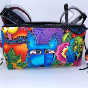 May include: A colorful zippered pouch with a whimsical design featuring cartoon dogs and flowers. The pouch has a black zipper, a black drawstring, and a silver key ring.