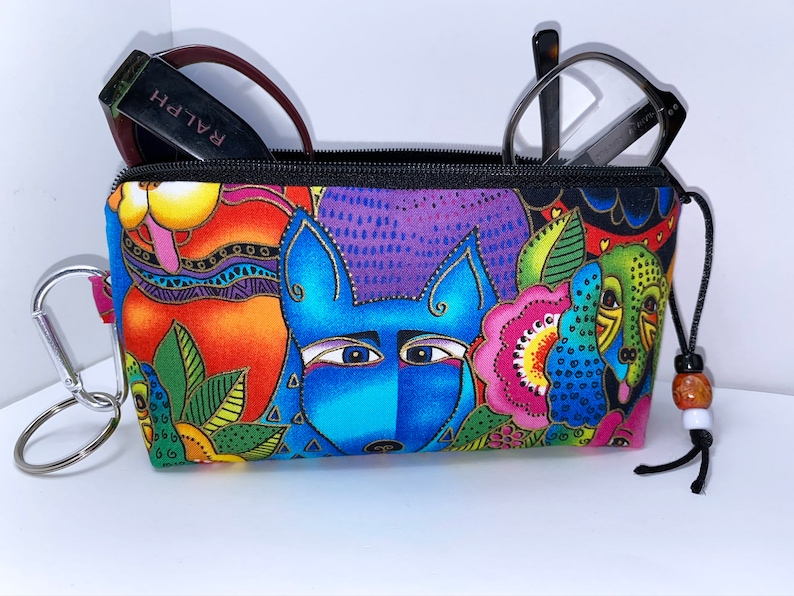 May include: A colorful zippered pouch with a whimsical design featuring cartoon dogs and flowers. The pouch has a black zipper, a black drawstring, and a silver key ring.