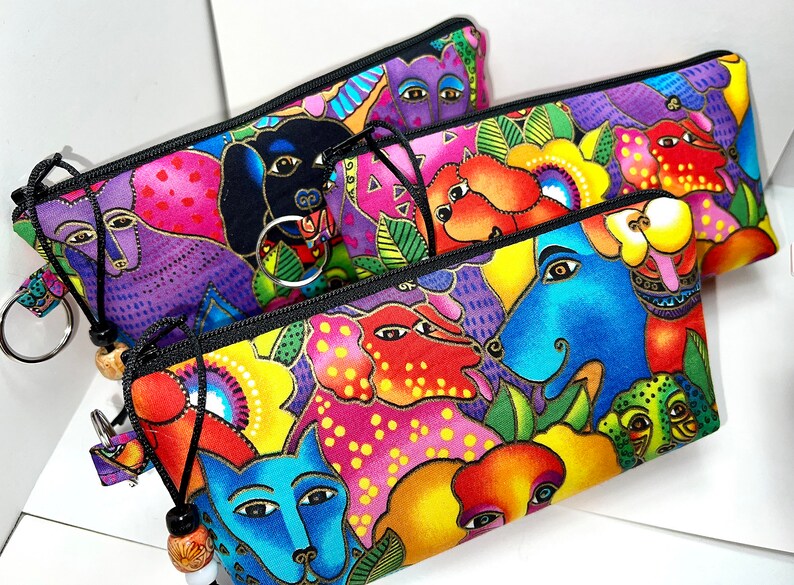 May include: Three colorful zippered pouches with a whimsical animal print design. The pouches feature a variety of colorful animals, including dogs, cats, and birds. The pouches are made of a durable fabric and have a zipper closure.
