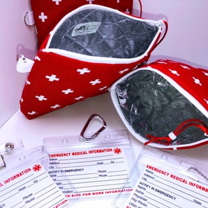 May include: Two red zippered pouches with white crosses and a silver zipper pull. The pouches are lined with a silver material. Two clear plastic card holders with the text "Emergency Medical Information" and spaces for name, address, city, state, zip, phone, and emergency contact information.