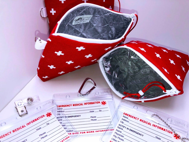 May include: Two red zippered pouches with white crosses and a silver zipper pull. The pouches are lined with a silver material. Two clear plastic card holders with the text "Emergency Medical Information" and spaces for name, address, city, state, zip, phone, and emergency contact information.