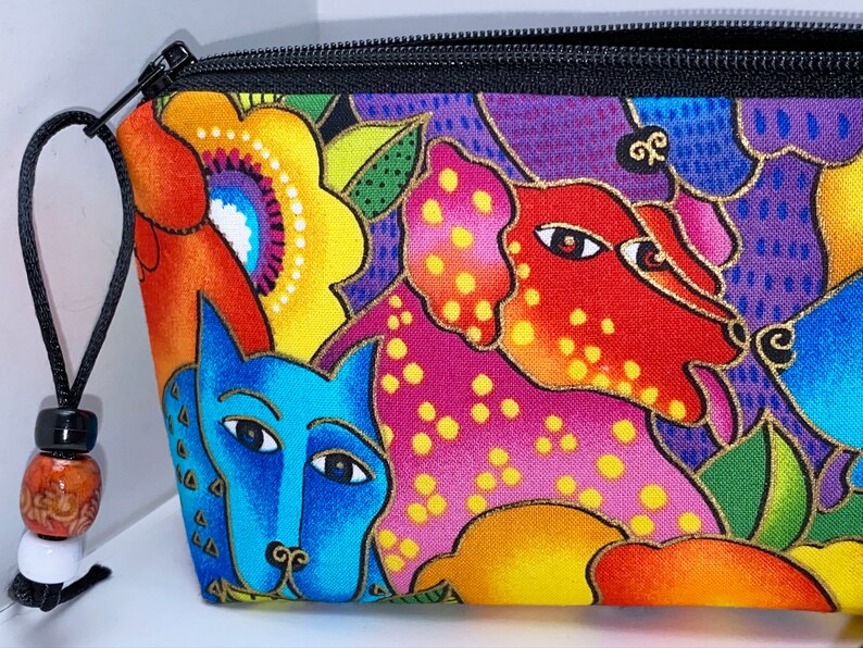 May include: A colorful zippered pouch with a black zipper and a black cord with beads. The pouch features a whimsical design of stylized dogs and flowers in shades of red, orange, yellow, green, blue, and purple.