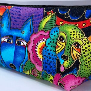 May include: A colorful zippered pouch with a blue wolf, green bird, and pink flower design. The pouch is made of fabric and has a black zipper.