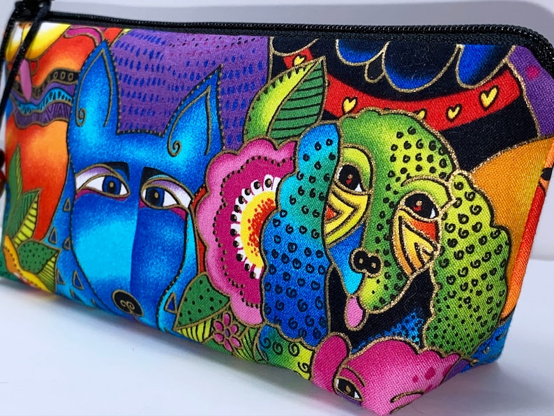 May include: A colorful zippered pouch with a blue wolf, green bird, and pink flower design. The pouch is made of fabric and has a black zipper.