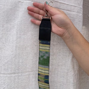 May include: A green, blue, and yellow patterned fabric strap with a black leather section and a silver metal clasp.