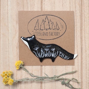 Pode incluir: Figura de raposa de cerâmica preta com detalhes brancos e dourados. A raposa está em pé sobre um fundo marrom com um logotipo que diz "Woodland Factory".