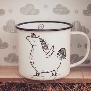 May include: White enamel mug with a black rim and handle. The mug features a black and white illustration of a unicorn with wings.