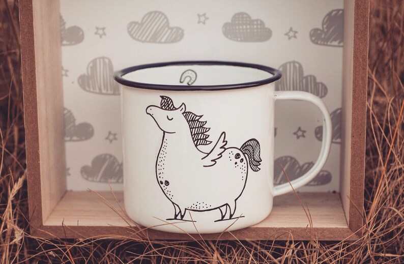 May include: White enamel mug with a black rim and handle. The mug features a black and white illustration of a unicorn with wings.