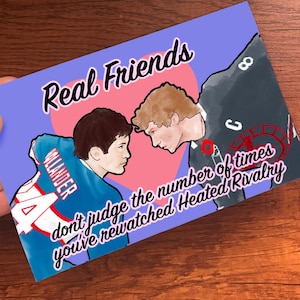May include: A greeting card with the words "Real Friends" in a script font. The card features illustrations of two people facing each other, with text that reads "don't judge the number of times you've rewatched Heated Rivalry."