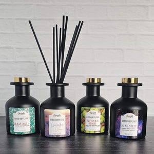 May include: Four black reed diffusers with gold-colored lids and labels. The labels read "Holly Jolly", "Lavender Lemon", "Welcome Home", and "Star Stuff". Each diffuser has black reeds inserted.