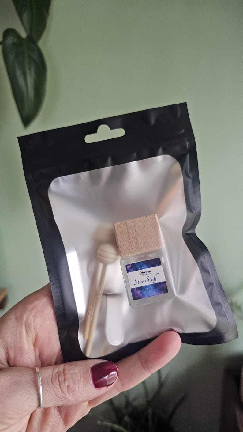 Puede incluir: Una botella transparente y cuadrada con una tapa de madera y una etiqueta que dice "Star Stuff" est&aacute; dentro de una bolsa de pl&aacute;stico transparente con un borde negro. La bolsa tambi&eacute;n contiene dos palitos de madera y una peque&ntilde;a cuchara de madera. El fondo es verde claro.