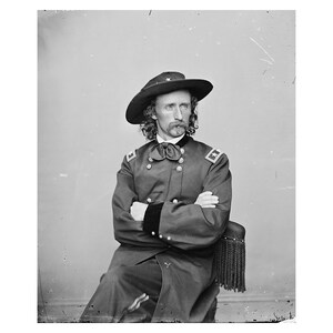 May include: A black and white portrait of a man in a military uniform. He is wearing a hat with a wide brim and has a mustache and beard. He is sitting in a chair with his arms crossed.