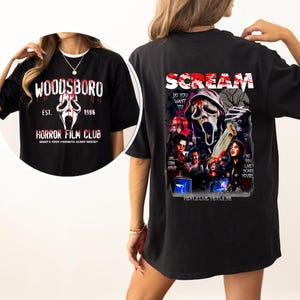 May include: Black t-shirt featuring a graphic from the movie Scream. The front of the shirt has the text "WOODSBORO HORROR FILM CLUB" with a ghost face graphic. The back of the shirt has the word "SCREAM" and other graphics.