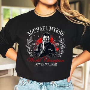 May include: Black sweatshirt with a graphic of Michael Myers holding a knife. The text "MICHAEL MYERS" is above the image, and "World Champion POWER WALKER" is below. The design includes the year "1980" and a decorative wreath.