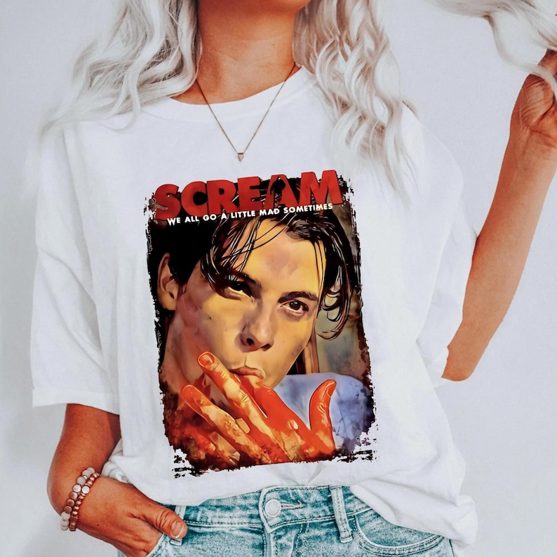 May include: White t-shirt featuring a graphic from the movie "Scream." The graphic includes the title in red letters and an image of a person with blood on their hands. The text "WE ALL GO A LITTLE MAD SOMETIMES" is also included.