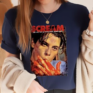 May include: Navy blue t-shirt featuring a graphic from the movie "Scream." The graphic includes the title "Scream" in red letters, the phrase "We all go a little mad sometimes," and a portrait of a person with blood on their hands.