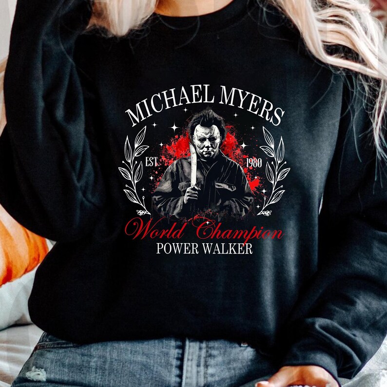 May include: Black sweatshirt with a graphic of Michael Myers holding a knife. The text "MICHAEL MYERS" is above the image, and "World Champion Power Walker" is below. The design uses red and white, with the year "1980".