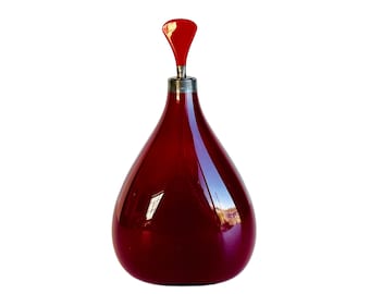 May include: A deep red glass bottle with a red glass stopper. The bottle has a rounded, teardrop shape.