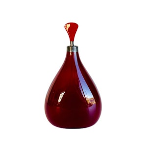 May include: A deep red glass bottle with a red glass stopper. The bottle has a rounded, teardrop shape.