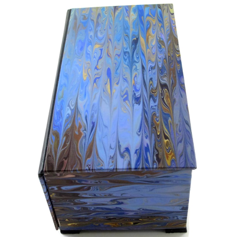 Puede incluir: Una caja de madera de color azul y marr&oacute;n con vetas de m&aacute;rmol y una tapa con bisagras. La caja tiene un patr&oacute;n de m&aacute;rmol decorativo en la parte superior e inferior.