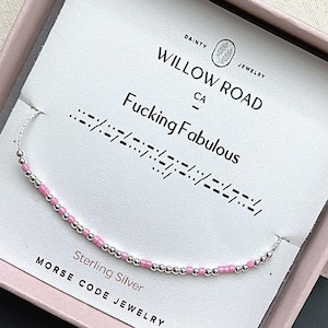 May include: A delicate bracelet featuring alternating small silver-toned metallic beads and light pink cylindrical beads. The bracelet is displayed on a white card printed with the text Willow Road Dainty Jewelry and Fucking Fabulous in Morse code.