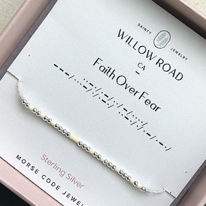 May include: A delicate bracelet featuring alternating silver-toned and cream-colored beads on a thin chain. The display card reads Willow Road CA, Faith Over Fear, and Sterling Silver, with Morse code symbols printed above the bracelet.