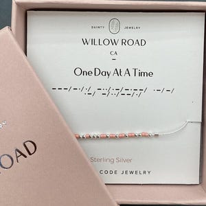 May include: A sterling silver code jewelry bracelet with pink and silver beads, presented in a pink box. The card inside reads "Willow Road CA One Day At A Time" with a Morse code message.