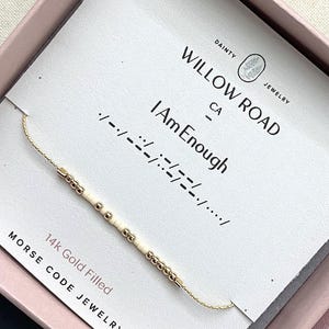 May include: A delicate gold-filled Morse code necklace with the message "I Am Enough." The necklace features small gold beads and white cylindrical beads. The card reads "Willow Road CA" and "Morse Code Jewelry."
