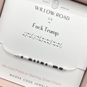 May include: A silver chain necklace with black and silver beads spelling out a message in Morse code. The necklace is displayed on a card with the text "Fuck Trump" and "Willow Road CA". The necklace is labeled as 14k Gold Filled or Sterling Silver Chain.
