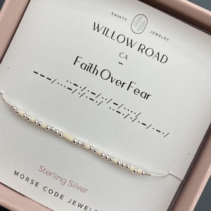 May include: A sterling silver Morse code necklace with the phrase "Faith Over Fear" spelled out in beads. The necklace is on a white card with the Willow Road Jewelry logo and text. The card is in a pink box.