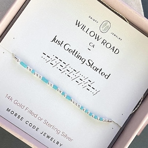 May include: A white ceramic mug with a black handle and the text "But First, Coffee" in a bold, black font. The mug is set against a blurred background, suggesting a cozy setting.