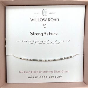 May include: A silver Morse code bracelet with the phrase "Strong As Fuck" spelled out in beads. The bracelet is on a white card with the Willow Road CA logo and text. The chain is 14k gold filled or sterling silver.