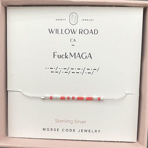 May include: A sterling silver Morse code bracelet with red and silver beads. The card behind the bracelet reads "Willow Road CA" and "FuckMAGA". The bracelet is presented in a pink box.