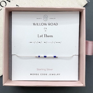 May include: A sterling silver Morse code bracelet featuring small metallic beads and blue cylindrical beads on a thin chain. The bracelet is displayed on a white card inside a pink box, with the text Willow Road CA, Let Them, and Morse Code Jewelry.