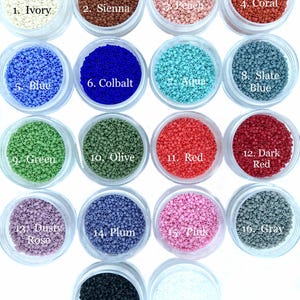 May include: Eighteen clear circular containers filled with small, cylindrical beads in various colors, labeled 1 through 18. Colors include ivory, sienna, peach, coral, blue, cobalt, aqua, slate blue, green, olive, red, dark red, dusty rose, plum, pink, gray, ebony, and white.