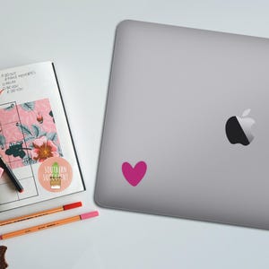 May include: A pink heart sticker is on a silver laptop. A planner with floral designs and the words "Goals this month" is open next to the laptop. There are also pens, a highlighter, and a sticker with the words "Southern Succulent".