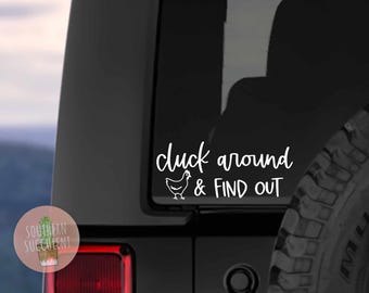 May include: A white vinyl decal applied to a dark vehicle window featuring a line drawing of a chicken and the text "cluck around & FIND OUT" in a combination of cursive and sans-serif fonts, positioned above a red taillight assembly.