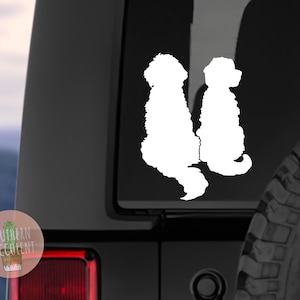 May include: White silhouette of two dogs sitting side by side on a black car. The dogs are facing forward and have fluffy tails.