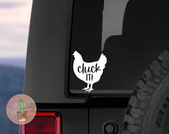 May include: A white vinyl decal applied to a vehicle window, featuring the silhouette of a chicken with the text "cluck IT!" written in a black script font across the center of the bird's body, creating a high-contrast graphic design.