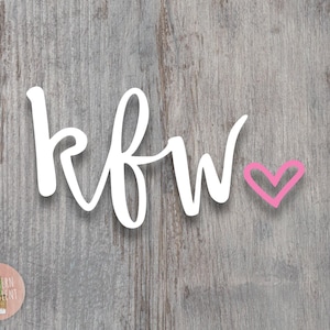 May include: A white script decal featuring the letters kfw in a lowercase cursive font, accompanied by a small pink hand-drawn heart symbol positioned to the right of the text. The design is presented against a weathered gray wood grain background.