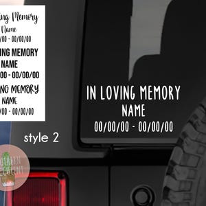 May include: A white vinyl decal for a vehicle window featuring the text IN LOVING MEMORY, a placeholder for a name, and a date range of 00/00/00 - 00/00/00. The decal is displayed on a dark vehicle surface with a spare tire visible.
