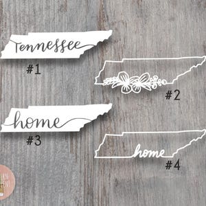May include: Four white vinyl decals shaped like the state of Tennessee. Design #1 features the word Tennessee in script. Design #2 shows a floral outline. Design #3 displays the word home in script. Design #4 features the word home in script.