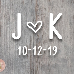 May include: White wooden sign with the letters J and K and a heart symbol between them. The date 10-12-19 is written below the letters.