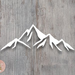 May include: A white vinyl decal featuring a stylized mountain range silhouette with sharp, jagged peaks and deep valleys. The design consists of a continuous outline of multiple mountain summits, creating a clean, minimalist graphic representation.
