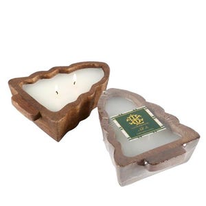 May include: Two-wick candle in a tree-shaped wooden container. The candle is white, and the wooden container is a warm brown color. The candle is next to a similar candle in plastic wrap with a green and gold label.
