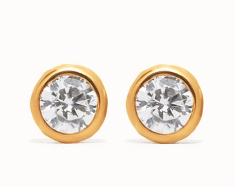 May include: A pair of gold stud earrings with a clear round stone in the center of each earring.