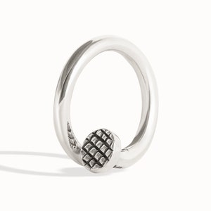 May include: A silver ring with a textured circular design on the band.