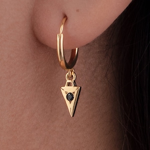 May include: Gold hoop earrings with a dangling triangle charm featuring a black gemstone in the centre.