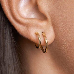 Puede incluir: Un par de pendientes de aro de oro, uno ligeramente m&aacute;s grande que el otro, usados en la oreja.